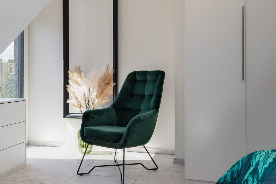 A standalone green velvet chair in a living room, styled with a small side table and minimal decor.