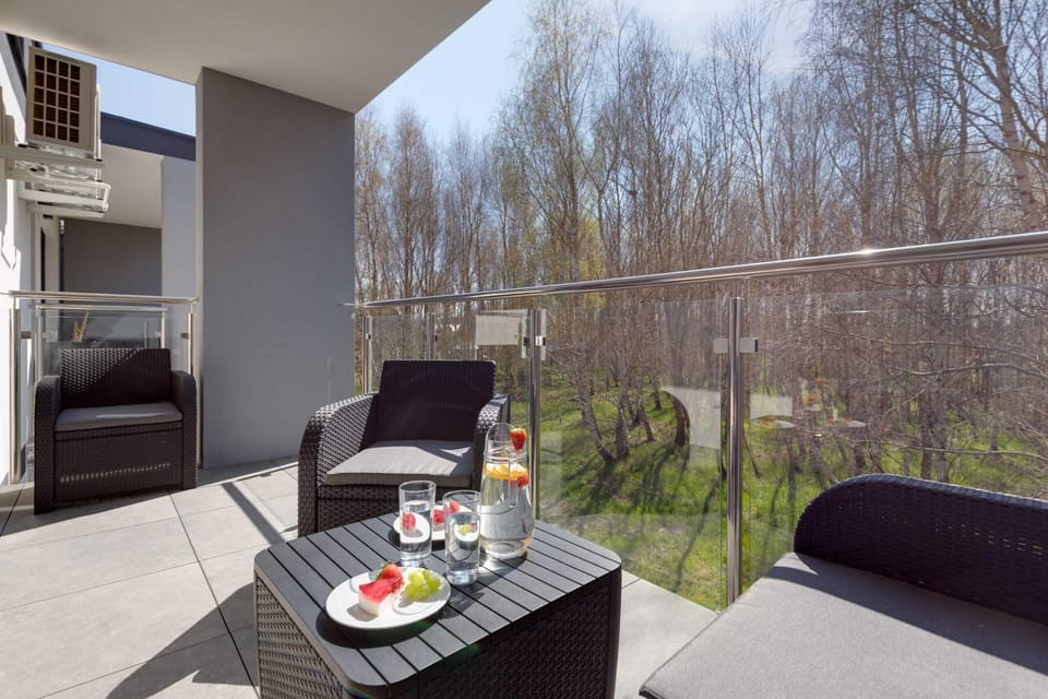 A balcony furnished with a table and chairs, offering a scenic view of trees and greenery.