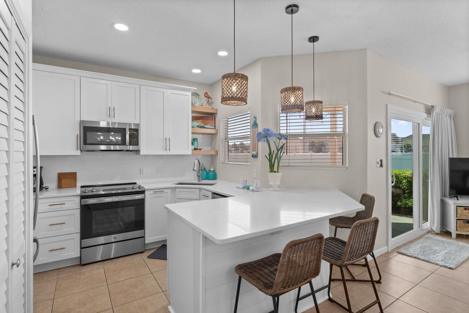 Your bright, modern kitchen awaits with pristine white countertops, pendant lighting, and stylish seating perfect for morning coffee or casual dining.