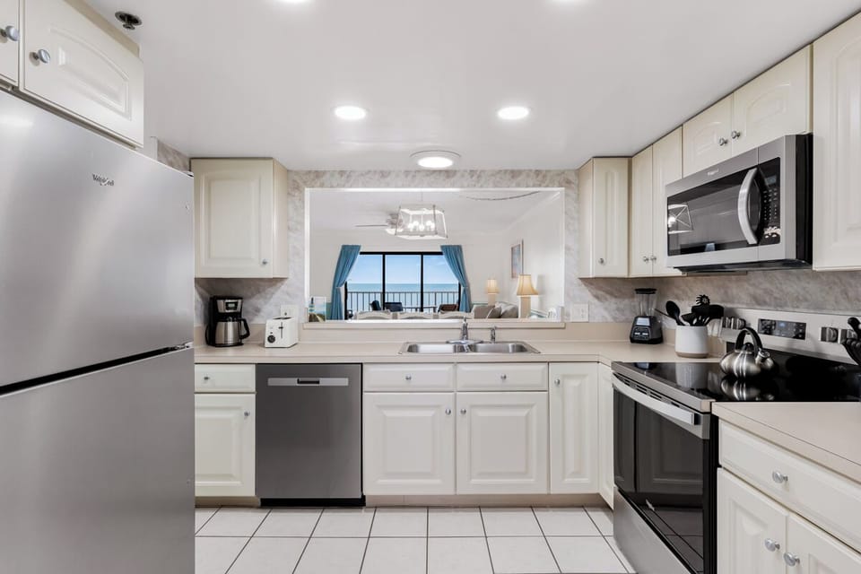 Your fully equipped kitchen features modern appliances and bright white cabinetry, with scenic ocean views beckoning through the living area.