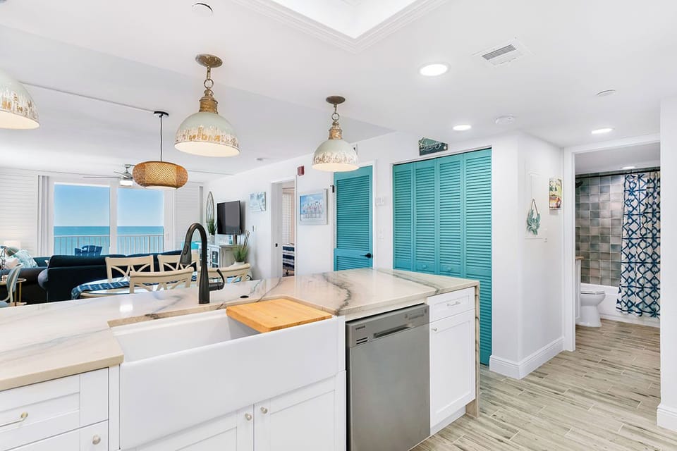 Your bright kitchen flows seamlessly into the living space, where turquoise shutters add coastal charm and ocean views create the perfect backdrop for cooking.