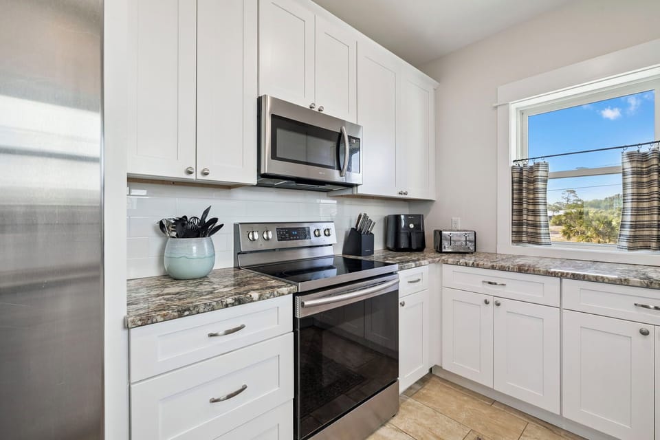 Prepare your favorite meals in this fully equipped kitchen with modern stainless steel appliances, granite countertops, and bright natural light streaming through the window overlooking scenic countryside views.