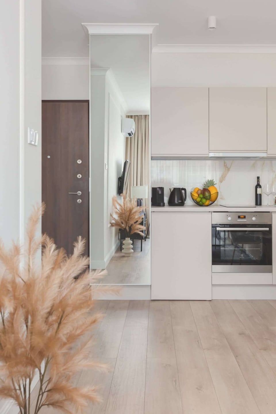 A view of the front door next to which is a large mirror and the kitchen area.