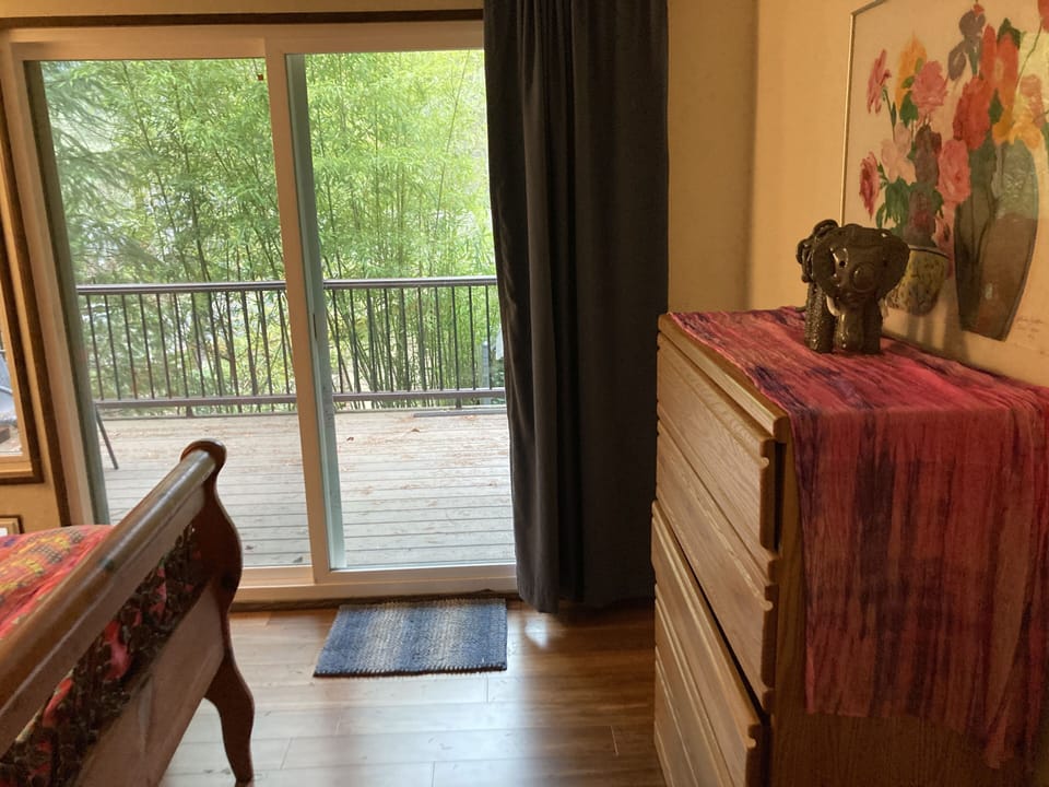 Master bedroom has a sliding glass door and a window looking out at the trees.