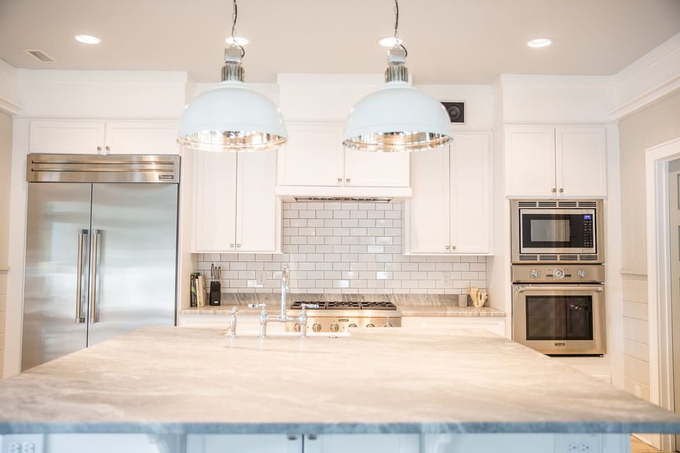 Modern kitchen with stainless steel appliances, white cabinets, tile backsplash, a large island, and two overhead lights.