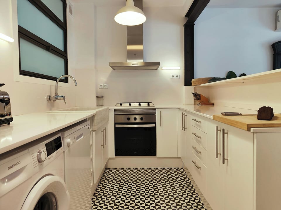 Fully equipped and open concept kitchen with a dishwasher, oven, stove, and a washing machine. The floor is made of black and white geometric tile.