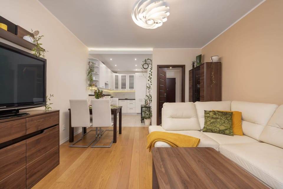 Living room view with a dining area, beige sofa, and bright wooden flooring.
