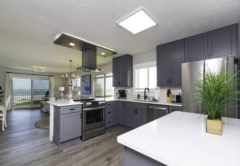 Gray shaker cabinets and stainless steel appliances surround white quartz countertops in the kitchen with ocean views.