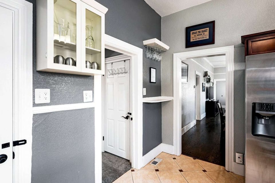 - Charming transition space features stemware racks and glass front cabinets
- Clean tile floors meet sleek dark wood for a stylish contrast in texture
- Wall art, shelf accents, and warm lighting complete the welcoming entry