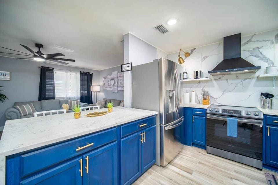 Prepare meals in this modern kitchen featuring a spacious marble island, sleek appliances, and cerulean blue cabinetry.