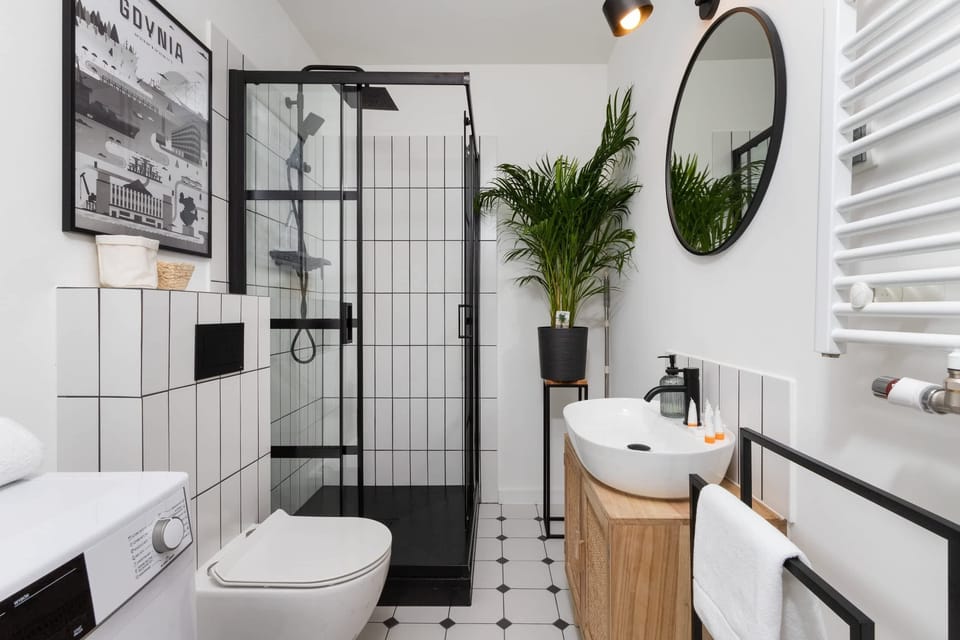 A sleek bathroom with a minimalist design, equipped with a washing machine, a round mirror, and black-framed glass shower doors for a contemporary look.