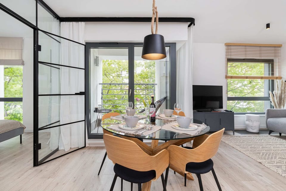 A beautifully set dining area with a round table, black chairs, and a large window, allowing ample sunlight to brighten the room.