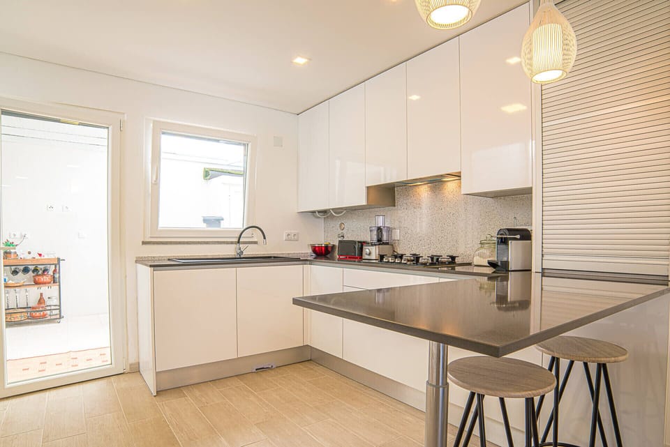 Modern white kitchen with dark grey island and bar seating — Villa Santi, luxury holiday villa in Aroeira
