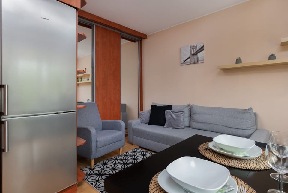 Modern kitchen corner with wooden cabinets, a fridge, and a dining table with tableware.
