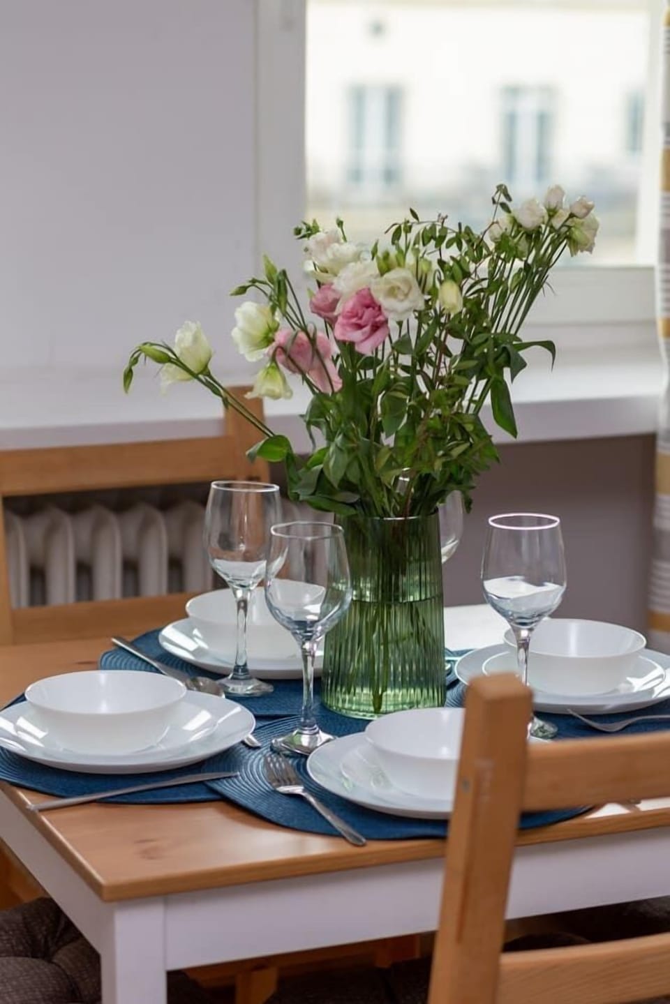 Close-up of a dining table set with flowers, elegant plates, and a bright window view.
