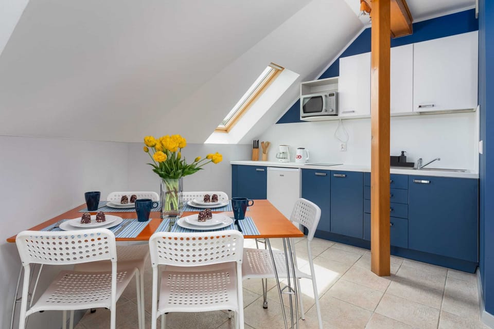 A bright dining area with a white table and chairs, situated next to a fully equipped kitchen with blue and white cabinets.
