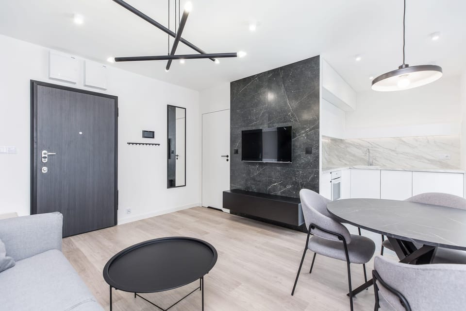 A minimalist dining and living area with sleek black accents, a cozy seating area, and light wooden floors, combining modern elegance with a comfortable atmosphere.