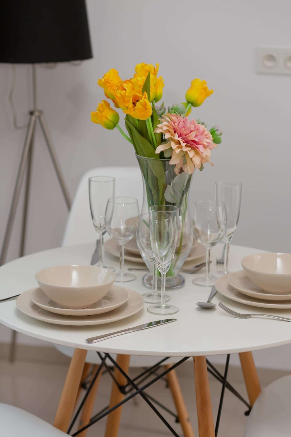 Close-up of a dining table featuring a vase of yellow flowers and neutral decor elements.
