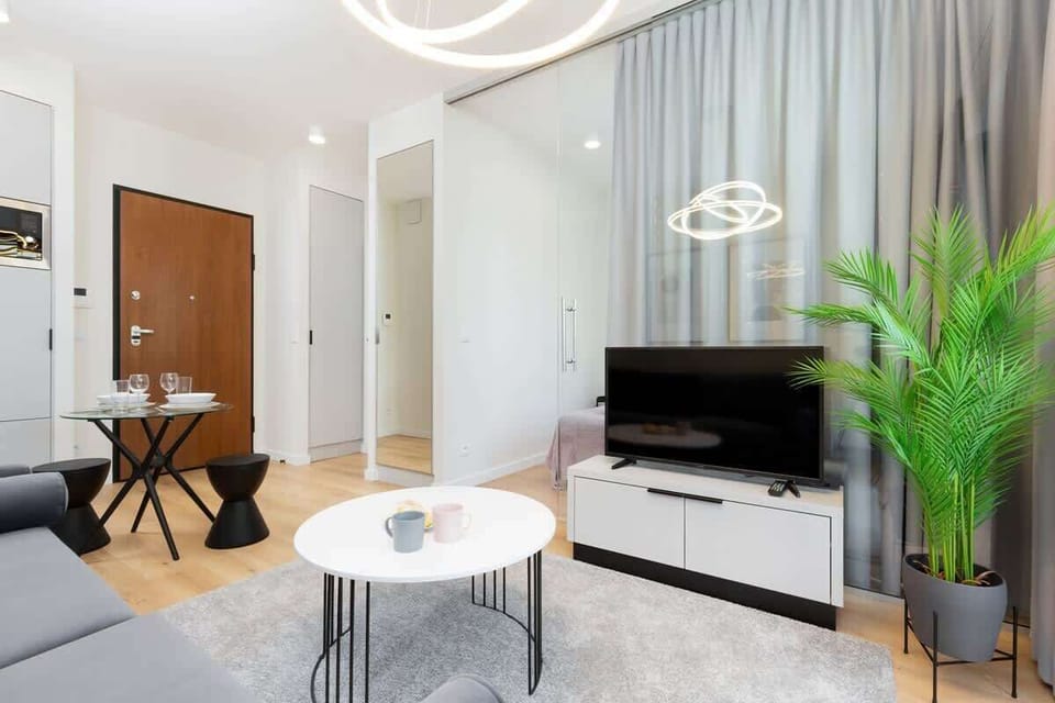 A spacious living room featuring a modern gray sofa, a white coffee table, and minimalist framed pictures on the wall. Bright colors and a large window add a sense of openness.