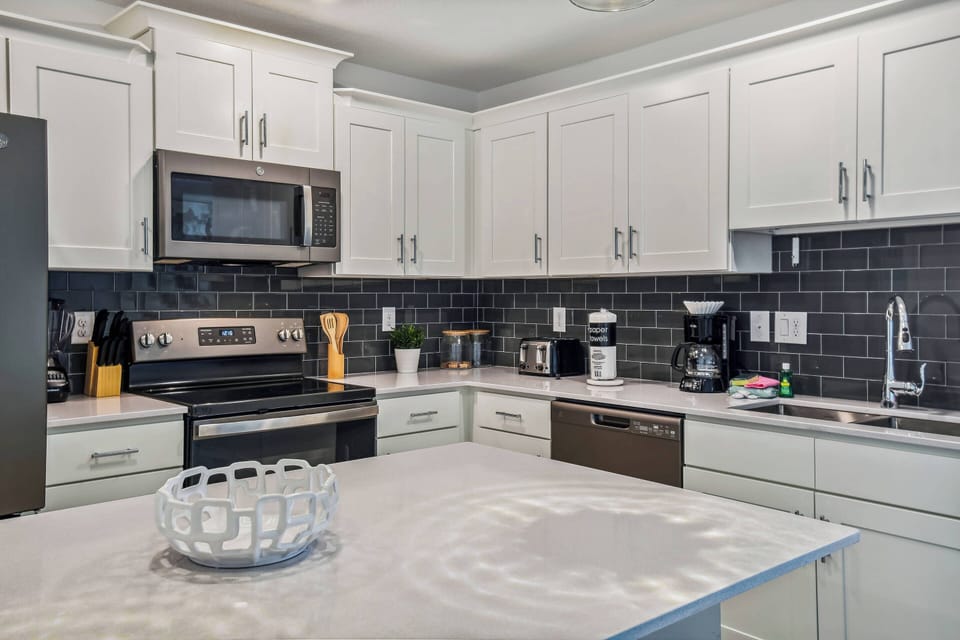 Welcome to this chic kitchen featuring sleek white cabinets and a striking black backsplash. The spacious island invites culinary creativity, while modern stainless steel appliances ensure your cooking experience is both stylish.