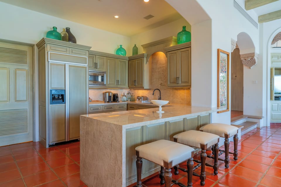 You'll love preparing meals in this elegant kitchen with a large center island, modern appliances, and warm terracotta tile floors that invite you to gather and create memories.
