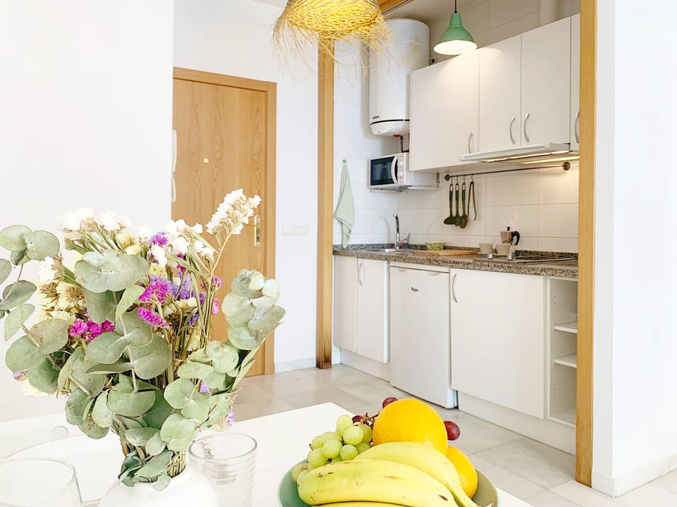 Living-dining room with equipped kitchen, stove, microwave, refrigerator, dish rack, and table for two.