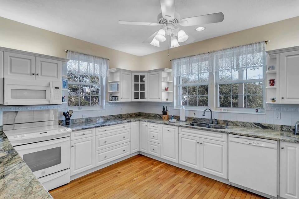 - Cook with ease in this charming corner kitchen featuring an electric stove, dual sink, and crisp finishes
- Three large windows bring in sunlight and frame views of the outdoors
- Ideal for families or longer stays with everything right at hand