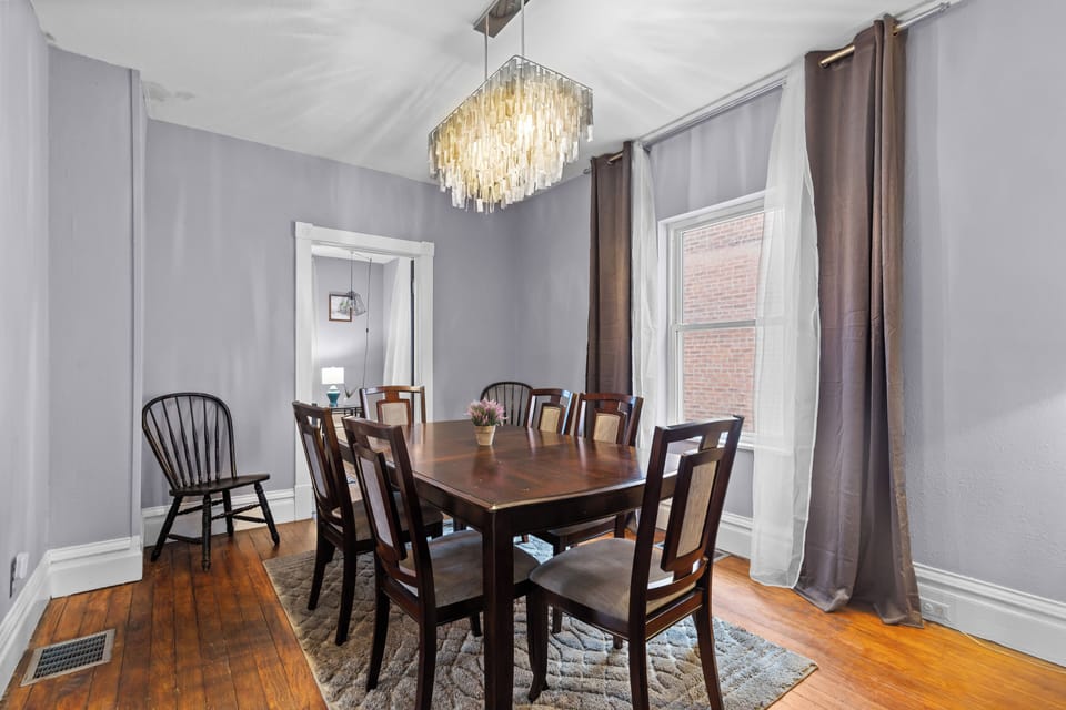 Opposite dining-room angle centered on the eight-seat table, chandelier, windows, and living-room doorway.