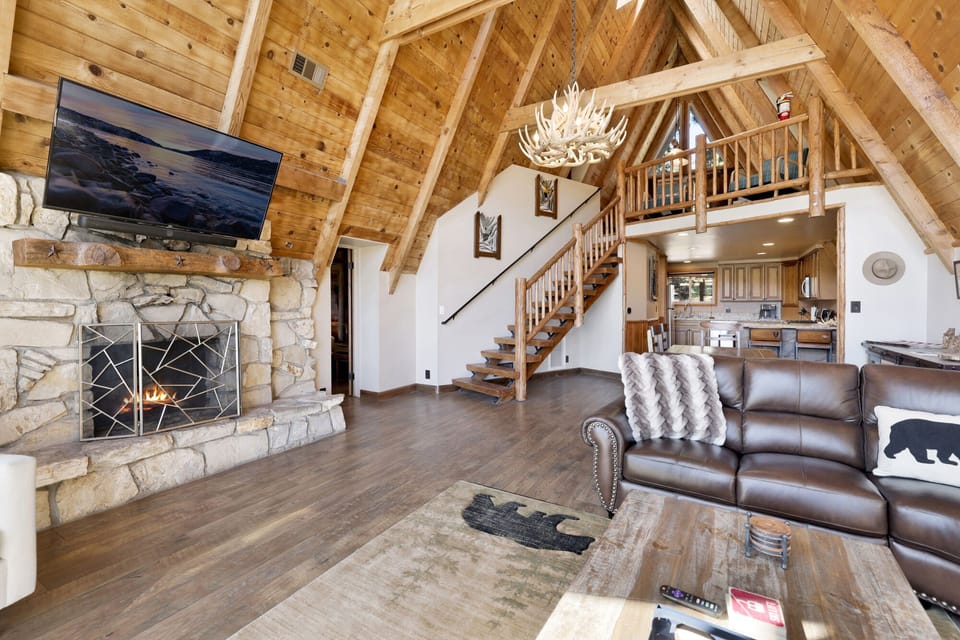 Cozy mountain living room with a stone fireplace, comfy seating, and smart TV—perfect for relaxing evenings, movie nights, and warm cabin vibes after outdoor adventures.