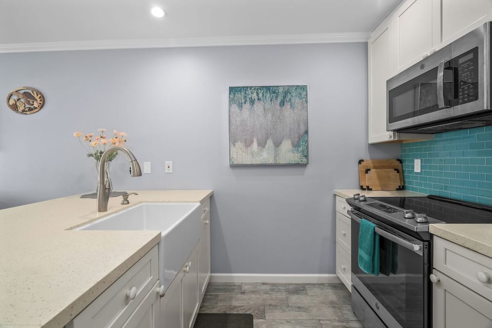 Your fully equipped kitchen features sleek white cabinetry, modern stainless appliances, and a vibrant turquoise backsplash that adds a refreshing coastal touch to your cooking space.