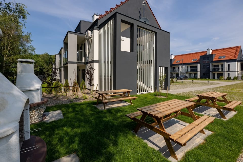 Outdoor seating space with picnic tables and a view of a residential building. 