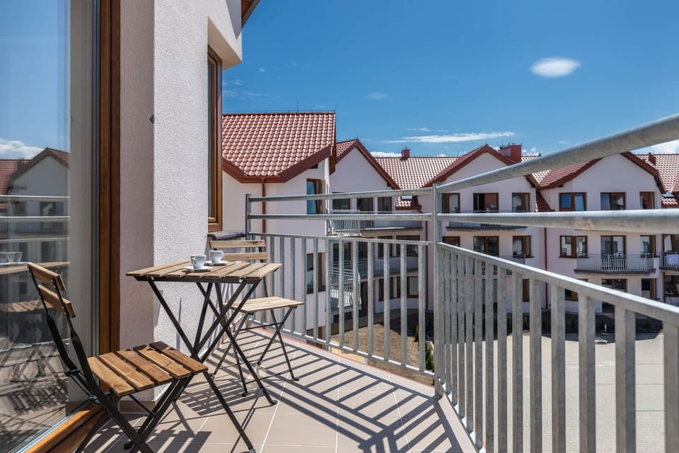 A view of a balcony with white railings and red rooftops. It overlooks a sunny residential area.
