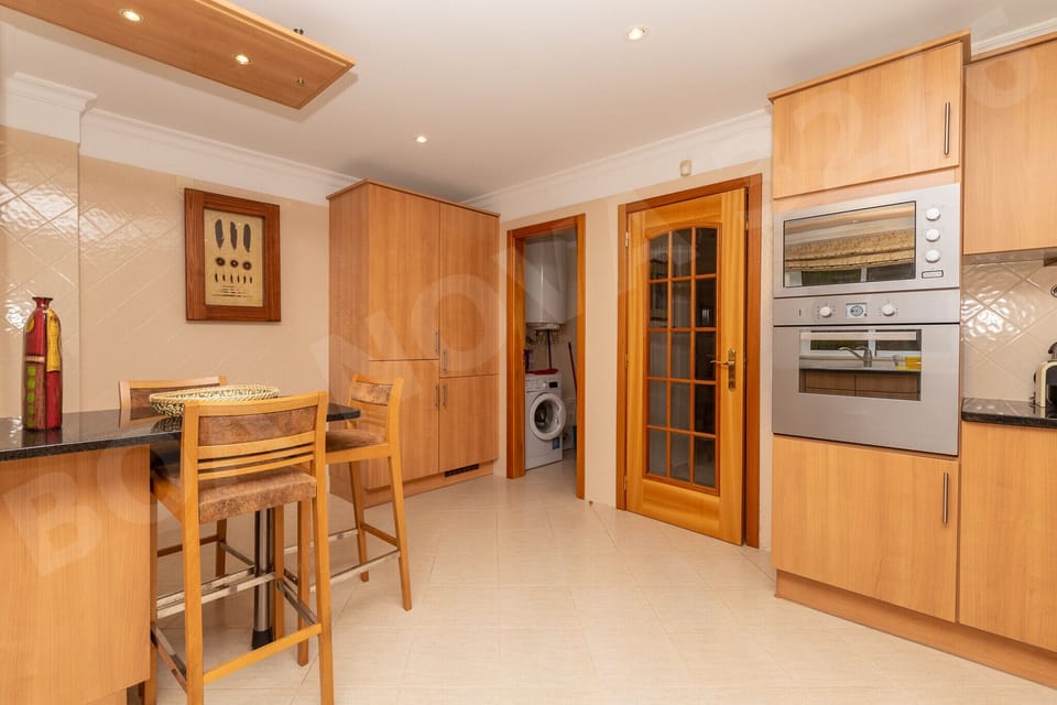 Well-equipped kitchen at Boa Nova 32/6 showing built-in double oven, wooden breakfast bar with stools and ample storage in the warm wooden cabinetry of this self-catering Vilamoura holiday apartment