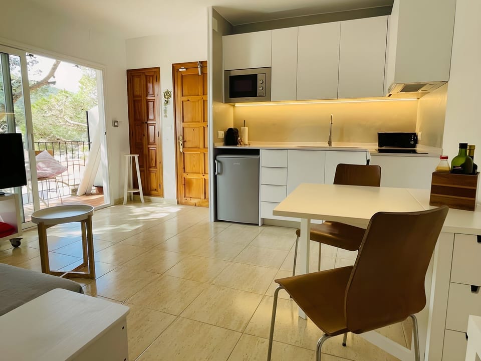 The bright and airy living space features a modern, fully equipped kitchen with white cabinets and a sleek countertop, perfect for preparing delicious meals during your stay. The tiled floors add a touch of elegance, while the sliding glass doors offer br