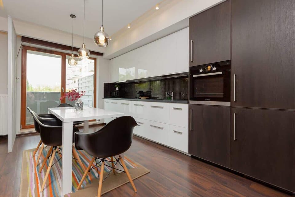 A spacious kitchen and dining area with a sleek white design, dark cabinets, and a large table surrounded by chairs.