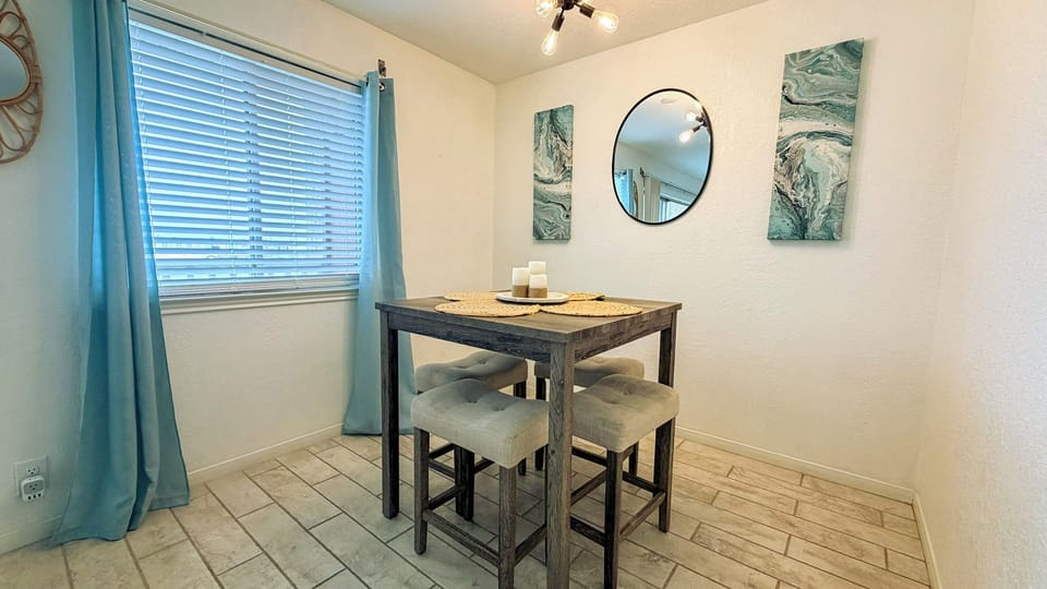 Gather around your cozy dining table for intimate meals, with soft morning light filtering through blue curtains and calming ocean artwork.