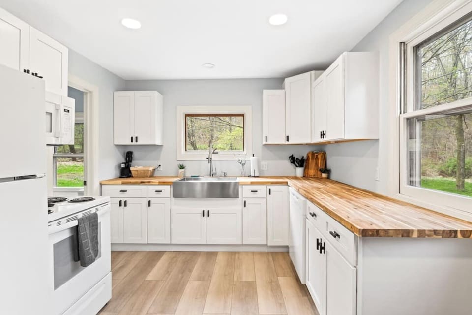 Whip up culinary delights in our bright, fully updated kitchen featuring pristine white cabinetry, stainless steel appliances, and a gorgeous wooden countertop with views of the tranquil outdoors.