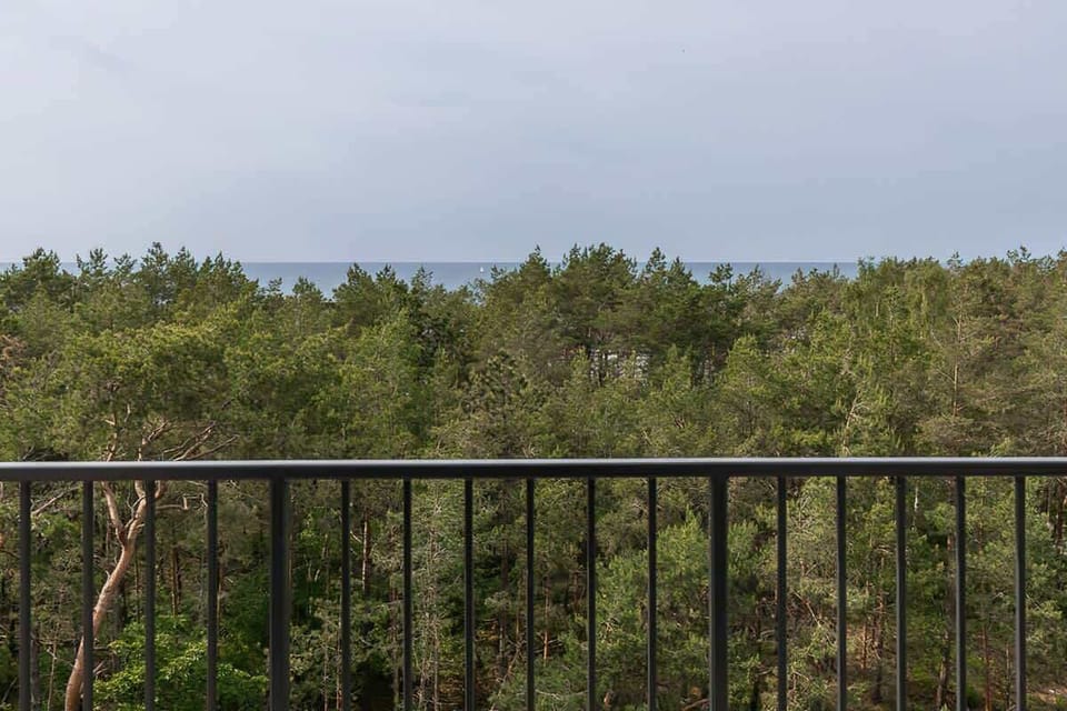A picturesque view of buildings nestled in greenery, with a hint of the sea in the distance.