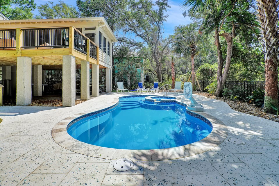 Dive into your private tropical oasis with this sparkling kidney-shaped pool, surrounded by lush palms and mature trees for ultimate relaxation.