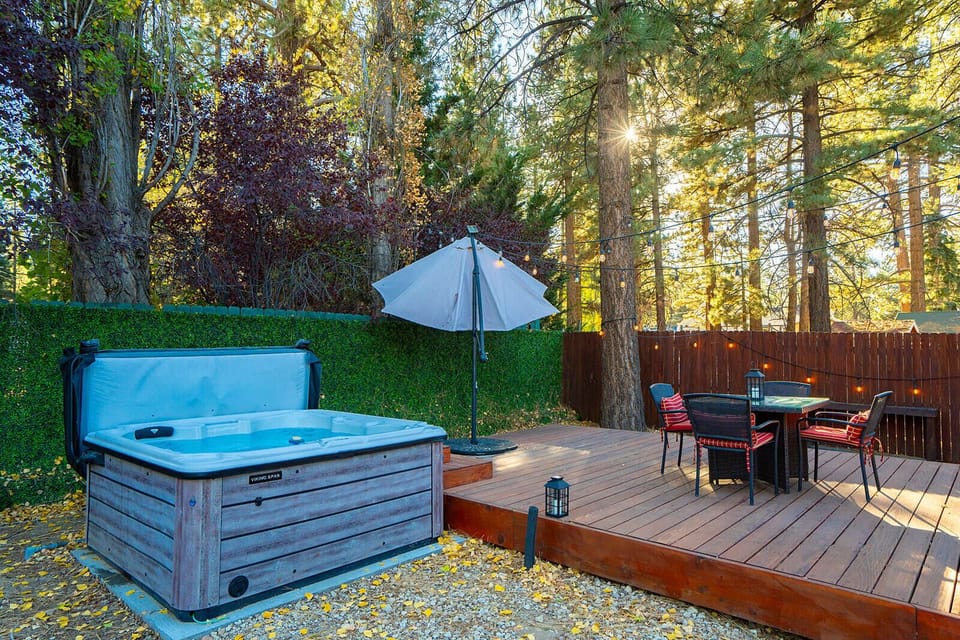 The redwood deck, table, umbrella, hot tub, and string lights among the trees