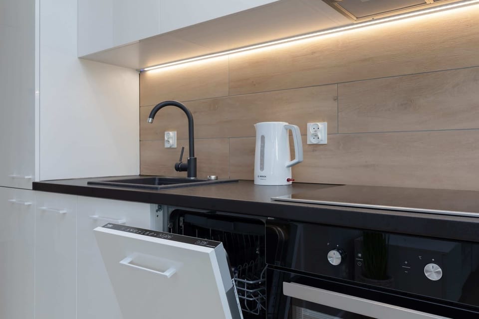 A modern black kitchen with an induction stove, black cabinets, and sleek backsplash lighting.