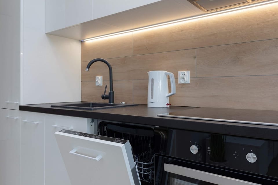 A modern black kitchen with an induction stove, black cabinets, and sleek backsplash lighting.