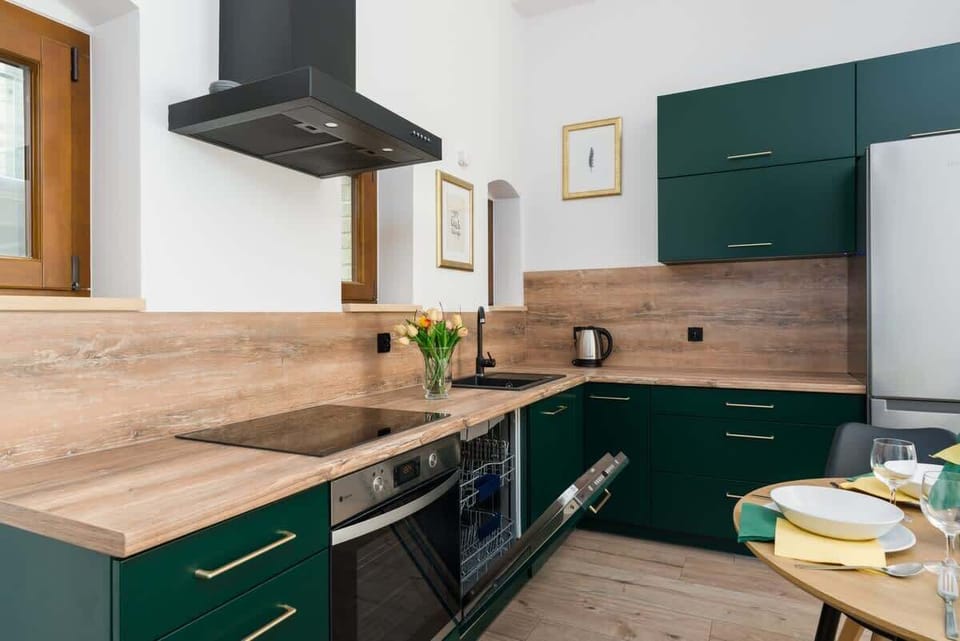 A modern kitchen with deep green cabinets, black fixtures, and a wooden countertop, combining elegance and functionality.