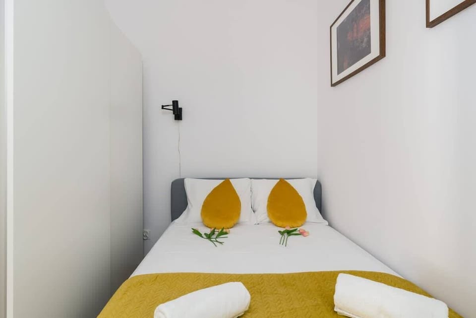 A cozy bedroom featuring a bed with white linens, mustard-yellow pillows, and wall art for added style.