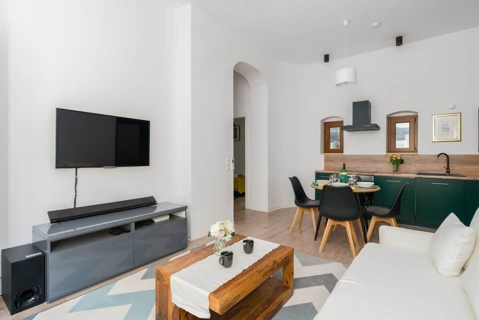 A bright, modern living room with a white sofa, wooden coffee table, and a TV mounted on the wall.