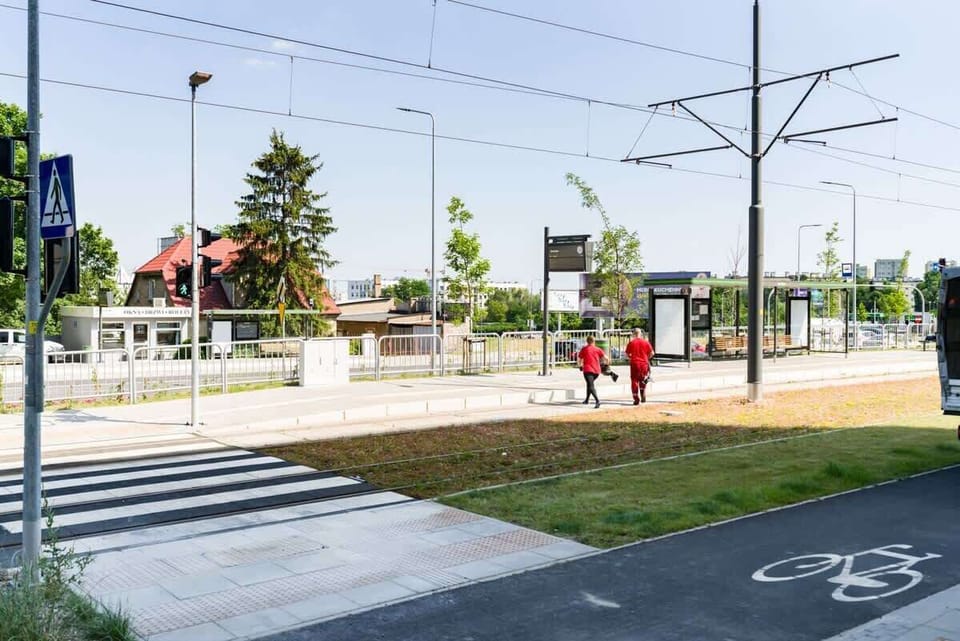 A street-level view of the neighborhood, featuring modern buildings, green areas, and a tram line.