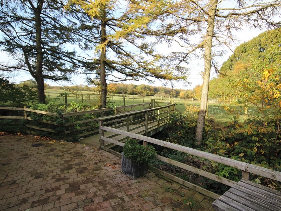 Paved patio with views through the trees to the play field and countryside beyond | Nuthatch Cottage - Wallace Lane Farm Cottages, Brocklebank, near Caldbeck and Uldale