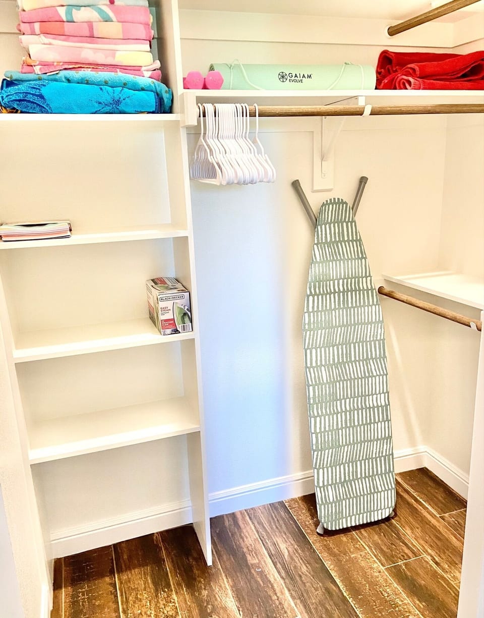 Walk-in closet with iron, ironing board, beach towels, yoga mat, & dumbbells.