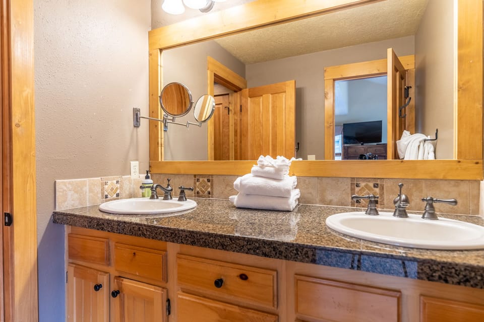 Pamper yourself in this elegant dual-sink bathroom featuring granite counters, warm wood cabinetry, and fluffy towels awaiting your arrival.