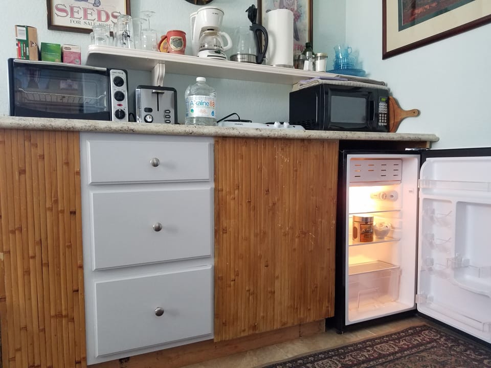 A kitchenette with microwave, toaster, oven, hotplate, pots, pans, refrigerator